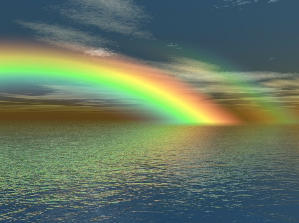 a rainbow above an ocean against a blue and cloudy sky