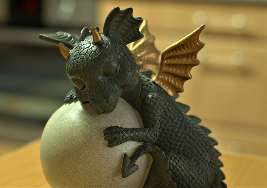 A tiny black dragon with golden wings, sleeping with an egg