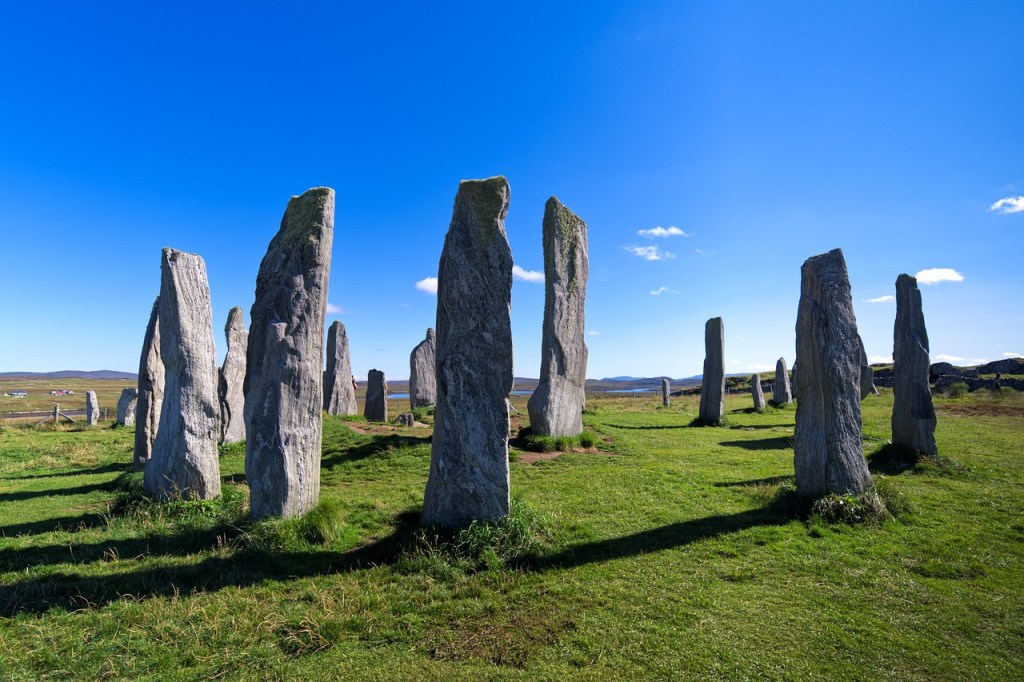 A circle of tall thin stones on green grass under a blue sky